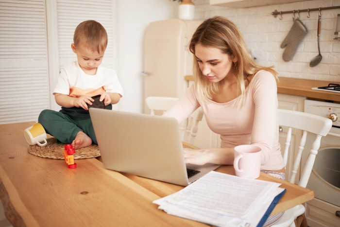 worried upset young blonde female sitting kitchen table with papers portable computer feeling stressed because she has make report take care her baby son while he is staying home