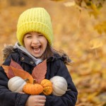little funny girl yellow hat with small pumpkins autumn forest blurred background copy space