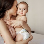 young tender happy mother hugging her newborn baby smiling sitting bed morning