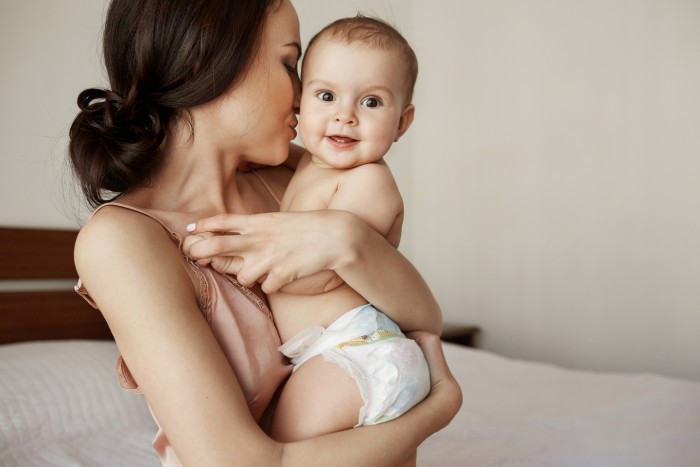 young tender happy mother hugging her newborn baby smiling sitting bed morning