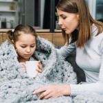 close up young mother taking care her sick daughter holding mug hand