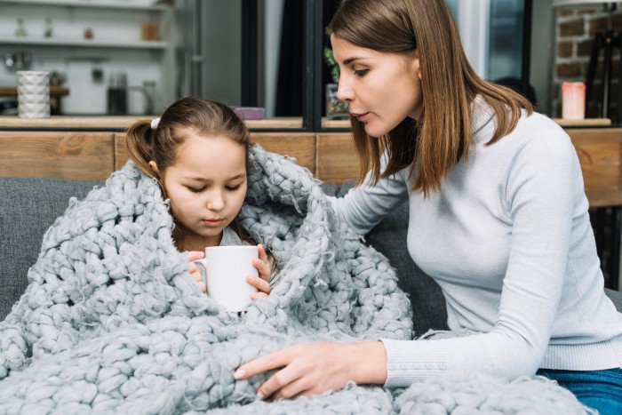 close up young mother taking care her sick daughter holding mug hand