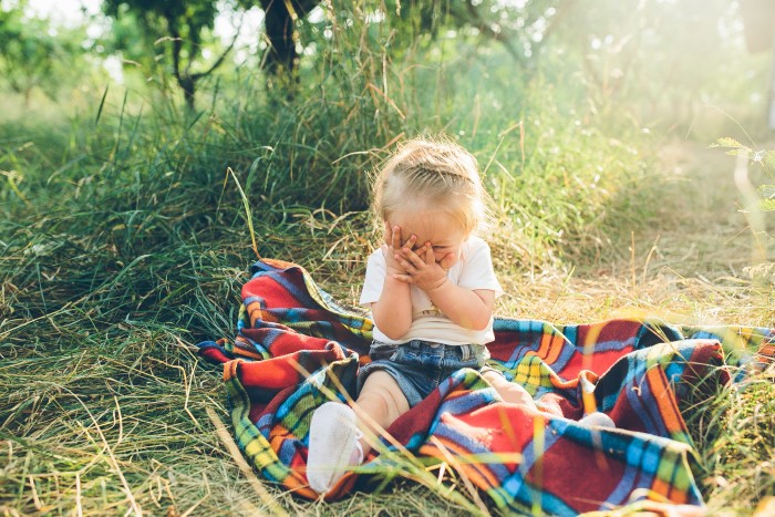 little girl covering her face sitting blanket floor